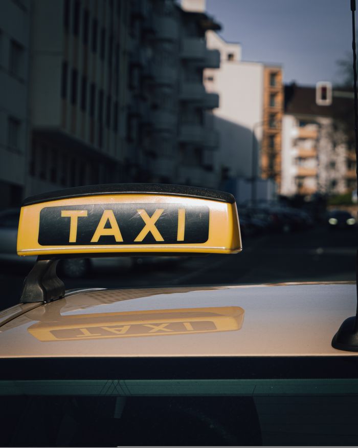 gallery-3 Close-up of a taxi sign on a car roof with an urban city background.