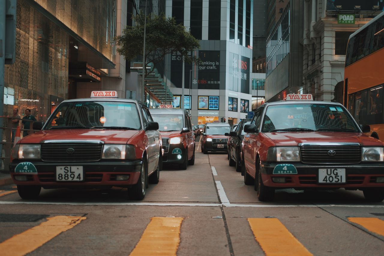 about-02 Red taxis driving through a busy downtown street in Hong Kong, showcasing urban life and vibrant city atmosphere.