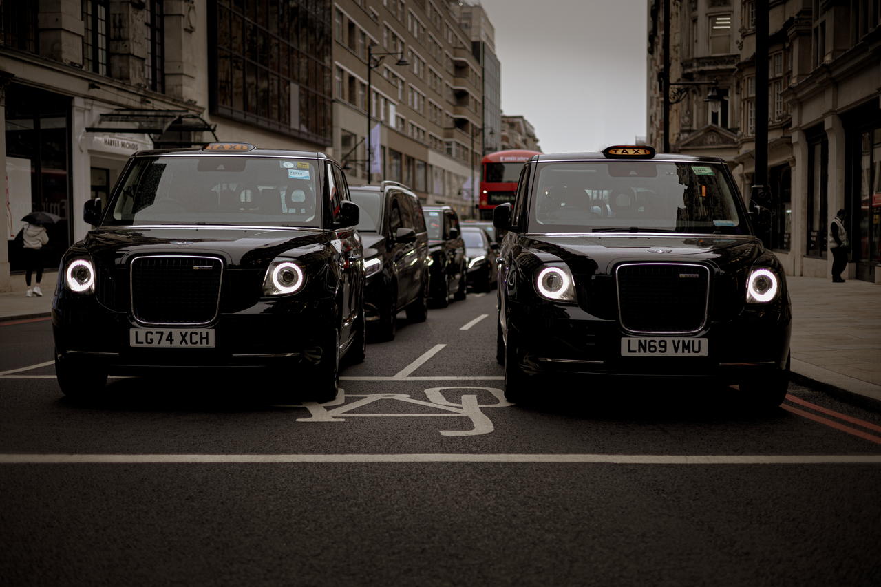 gallery-1 Black taxis line up on a London street showcasing modern urban transportation.