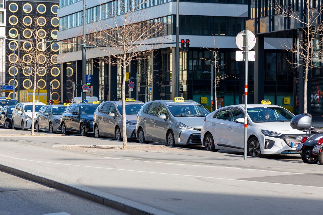 about-01 A lineup of taxis on an urban street with modern buildings in the background.