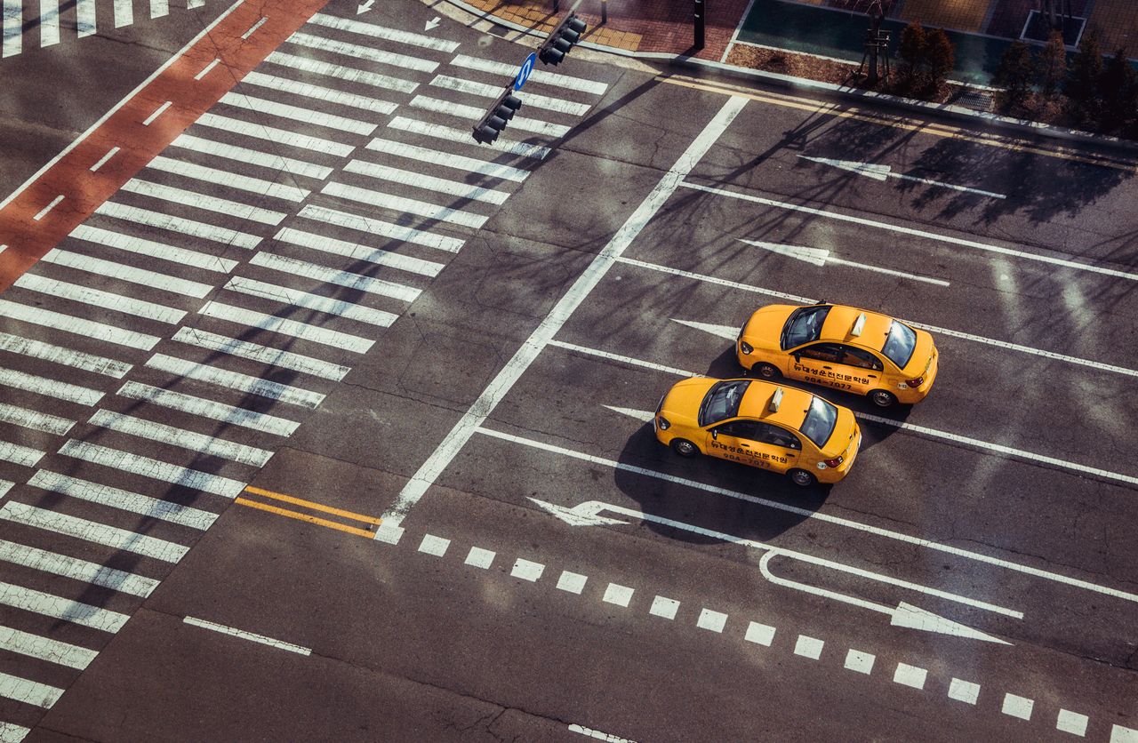services-01 Two yellow taxis navigate a city intersection with marked pedestrian crossings.