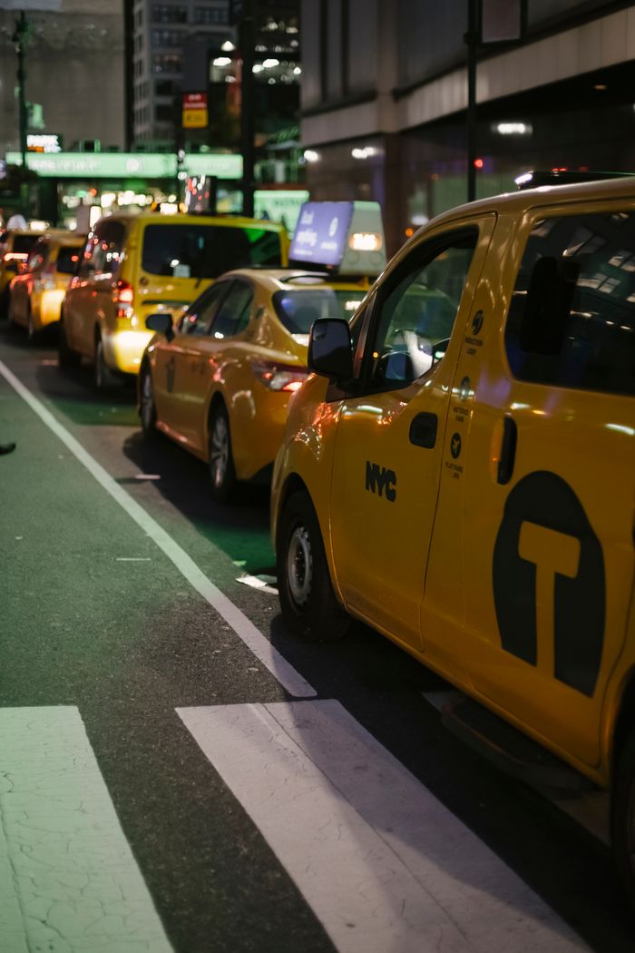 services-03 Row of modern various yellow taxi vehicles parked on city street near buildings in New York at night